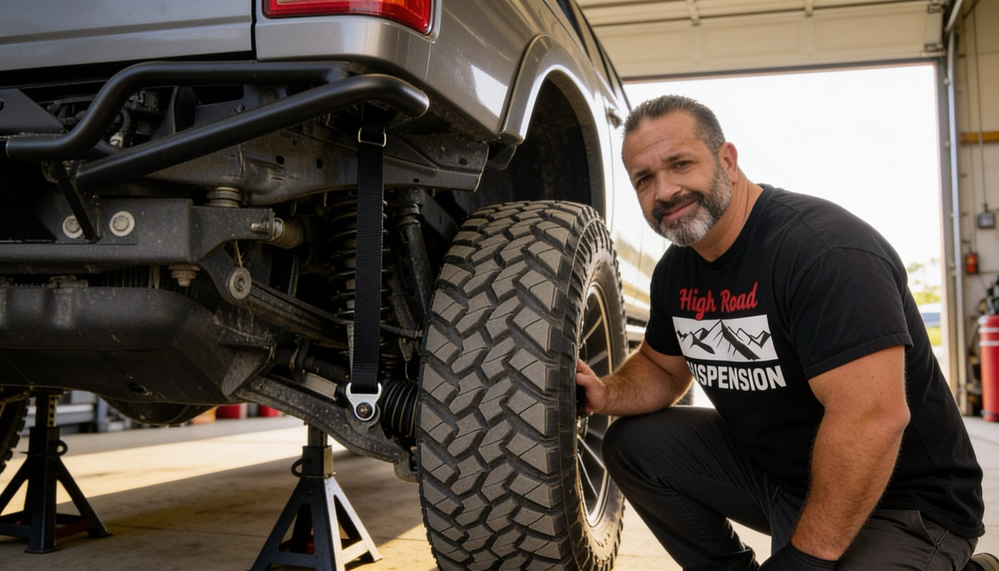 Black limit strap connecting the frame to the rear suspension of a lifted truck on jack stands in a HIGH ROAD Suspension shop.
